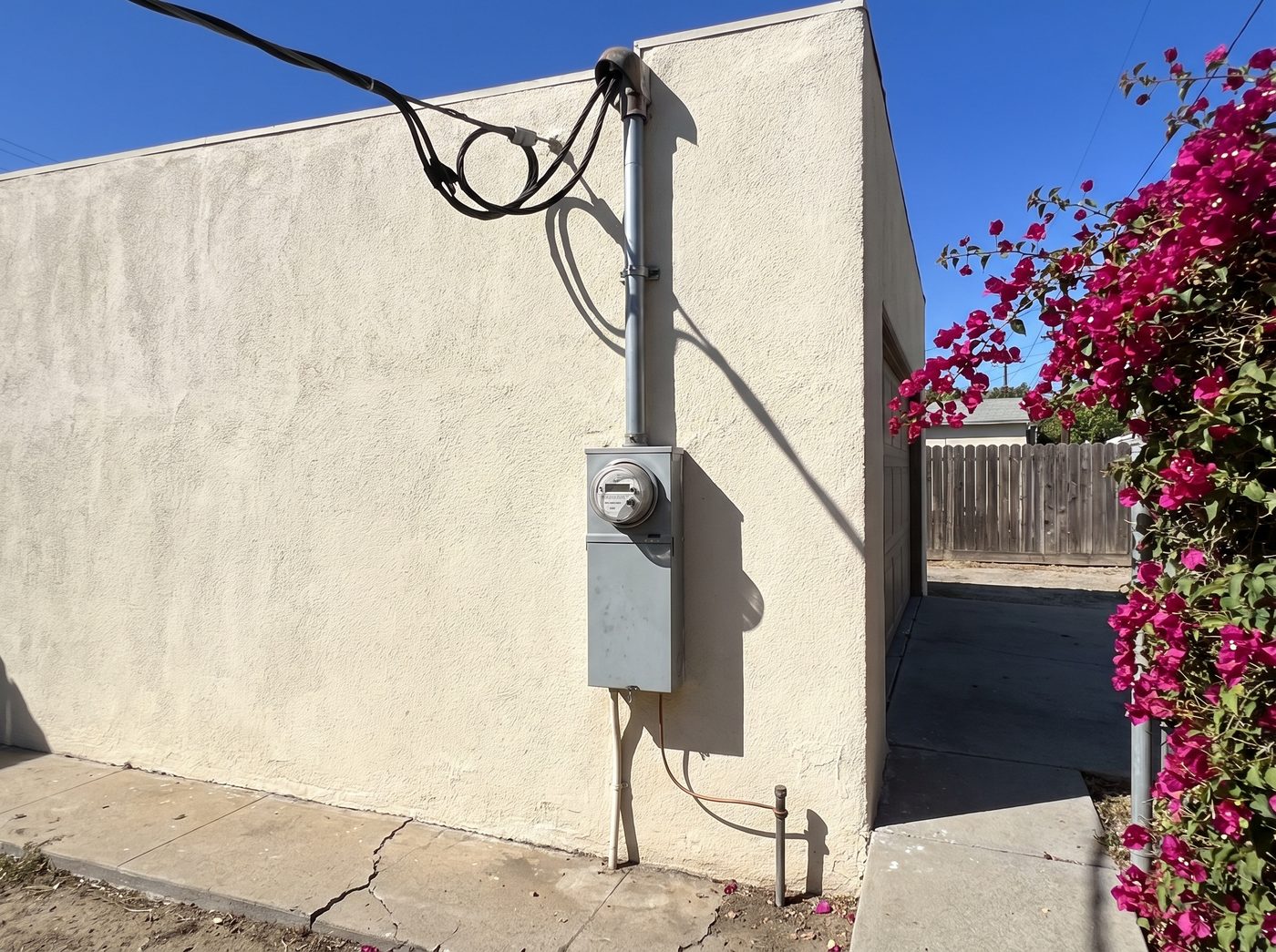 A residential service entrance on a stucco wall: the overhead drop and weatherhead at the top, the sealed meter socket below it, and the main disconnect beneath that.